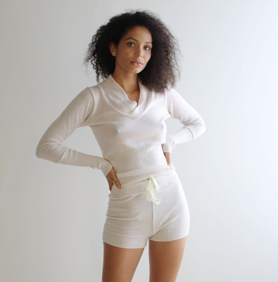 May include: A white long-sleeved shirt with a scoop neck and a white pair of shorts with a drawstring waist.